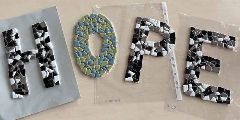 Kreatives Mosaikprojekt mit Schülerhand beim Legen blauer Keramiksteine